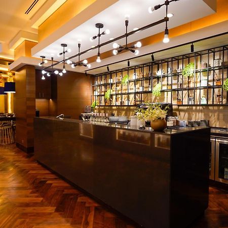 Jabal Omar Hyatt Regency Makkah Hotel Mekka Kültér fotó The photo shows a modern bar area in a restaurant. The bar features a sleek, dark countertop and is backed by a decorative arrangement of shelves that holds various bottles and plants. The lighting is warm and stylish, with multiple hanging pendant l