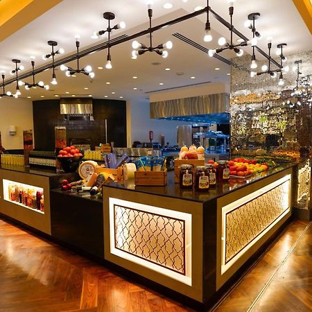 Jabal Omar Hyatt Regency Makkah Hotel Mekka Kültér fotó The photo shows a stylish and modern buffet area in a restaurant or hotel. The design features a sleek counter with various food items displayed, including fresh fruits. The space is well-lit with pendant lights hanging from the ceiling, creating a w