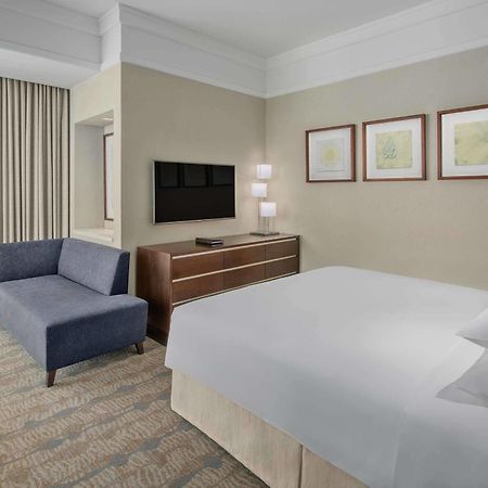 Jabal Omar Hyatt Regency Makkah Hotel Mekka Kültér fotó The photo shows a modern hotel room featuring a neatly made bed with white linens, a small blue couch to the side, and a wooden dresser with a television mounted on the wall above it. There are two framed pieces of art on the wall near the bed, and t