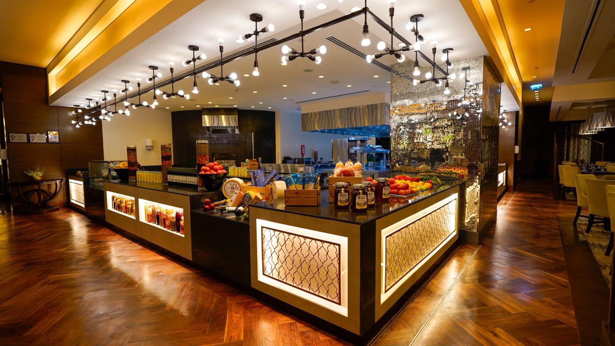 Jabal Omar Hyatt Regency Makkah Hotel Mekka Kültér fotó The photo shows a stylish and modern buffet area in a restaurant or hotel. The design features a sleek counter with various food items displayed, including fresh fruits. The space is well-lit with pendant lights hanging from the ceiling, creating a w