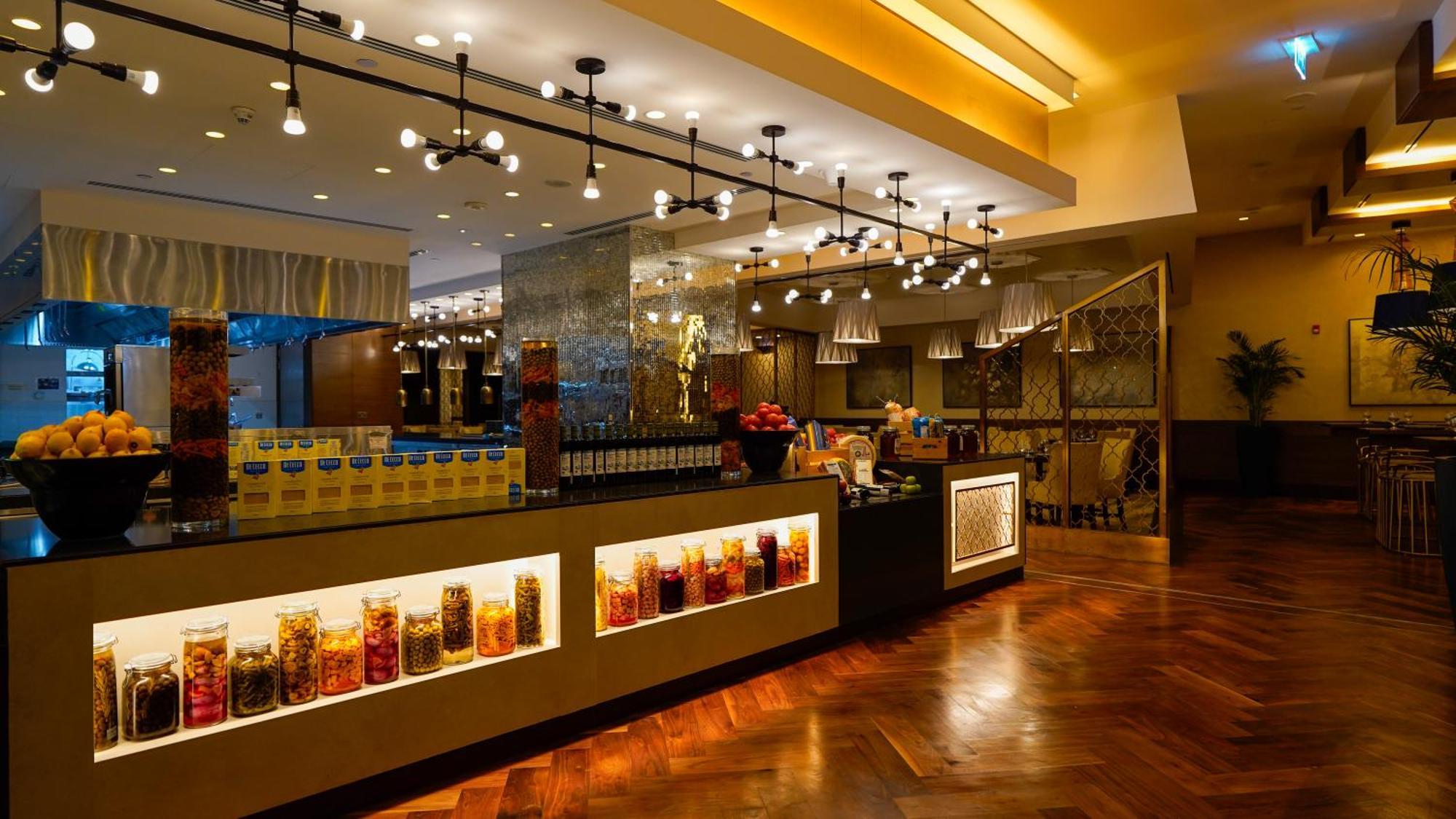 Jabal Omar Hyatt Regency Makkah Hotel Mekka Kültér fotó The photo shows a stylish interior of a restaurant or café. It features a well-lit space with modern lighting fixtures hanging from the ceiling. The focal point is a counter area with jars filled with colorful ingredients or snacks, illuminated by li