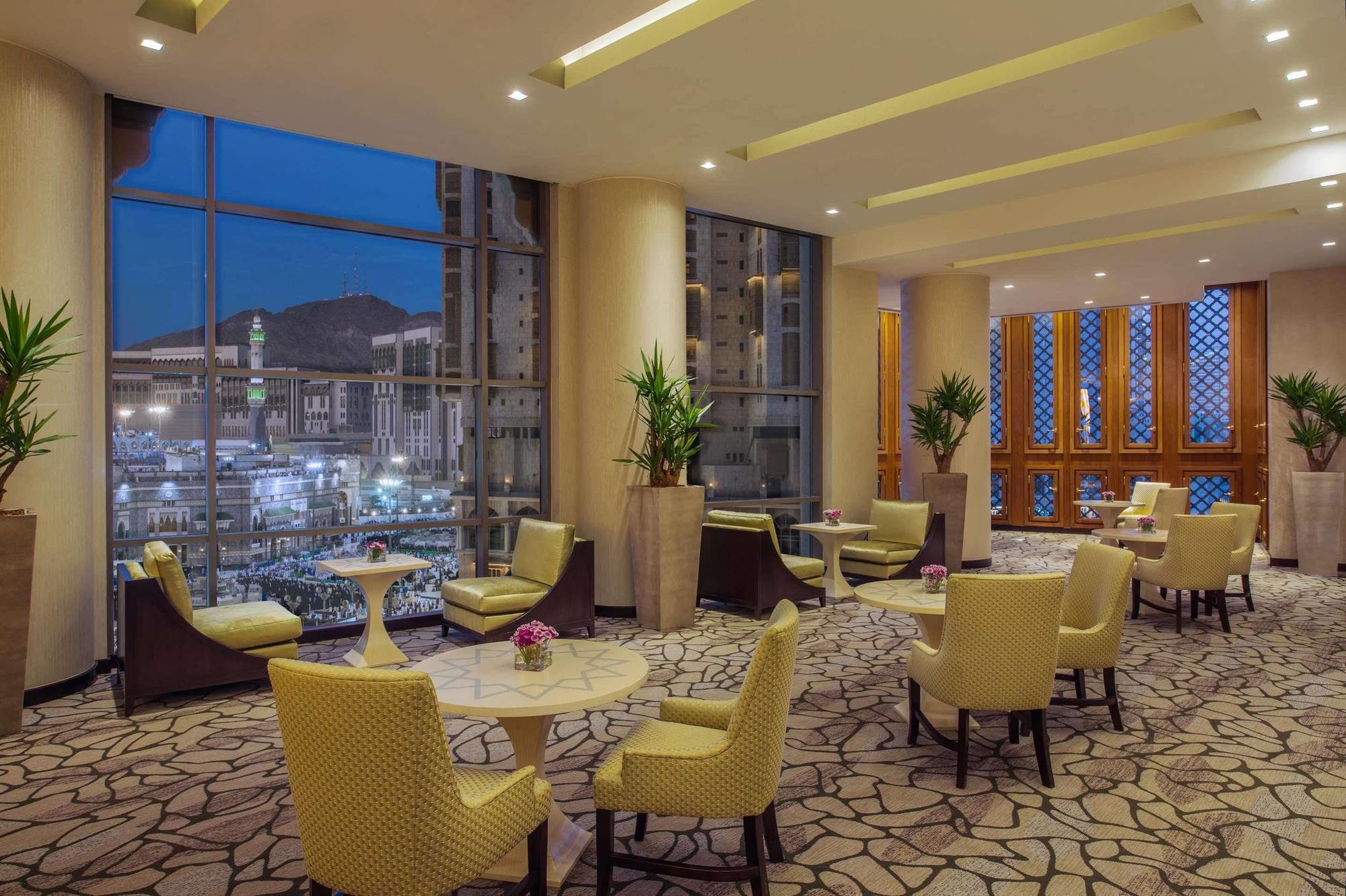 Jabal Omar Hyatt Regency Makkah Hotel Mekka Kültér fotó The photo shows a stylish lounge area, likely located in a hotel or café. It features several comfortable seating arrangements with light-colored chairs and small tables. The space is well-lit with modern lighting and has large windows that offer a v