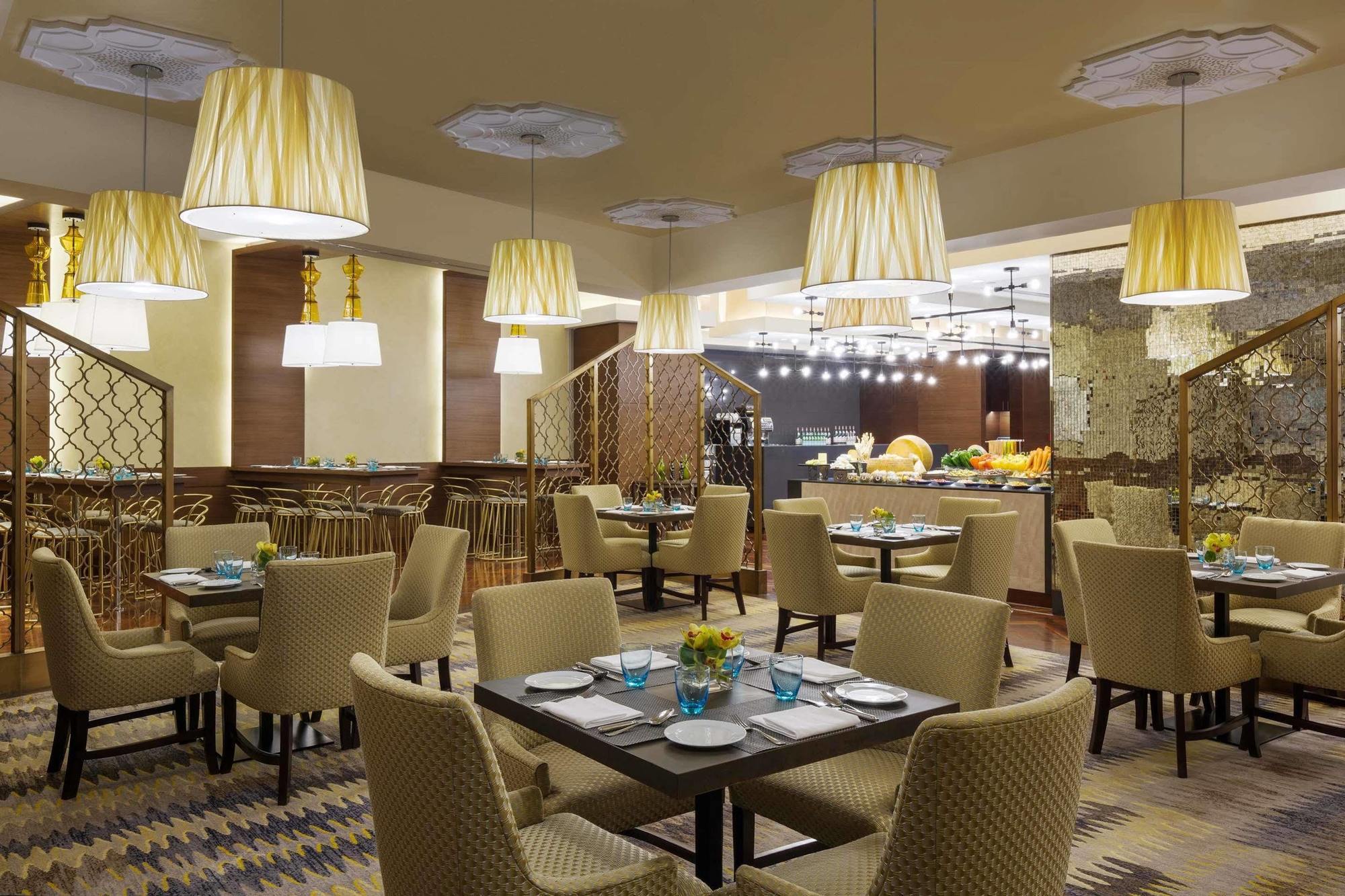 Jabal Omar Hyatt Regency Makkah Hotel Mekka Kültér fotó The photo displays a modern restaurant interior. It features a series of round tables with beige upholstered chairs arranged neatly throughout the space. Each table is set with plates and blue-tinted glasses. The lighting is provided by stylish penda