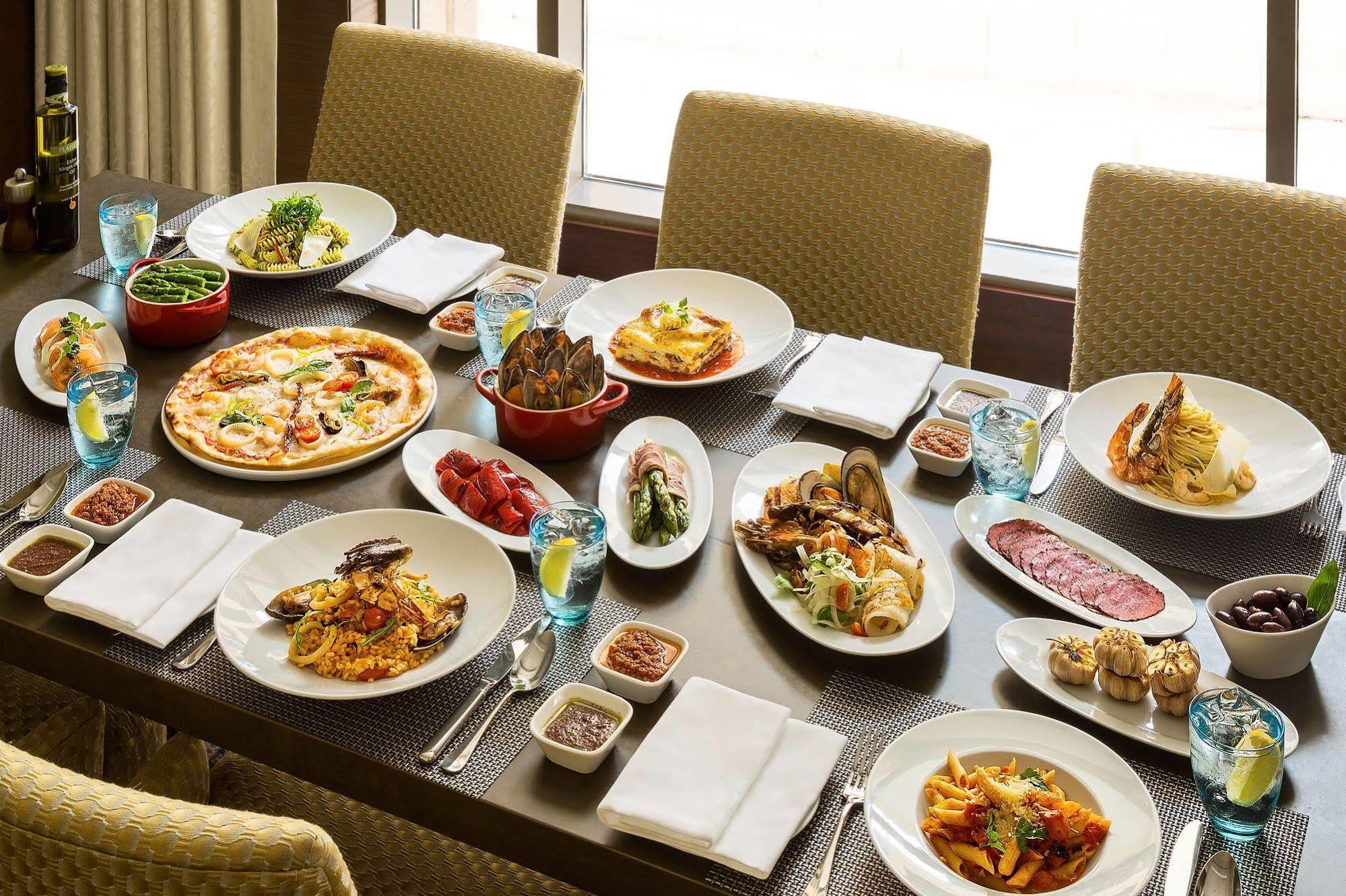 Jabal Omar Hyatt Regency Makkah Hotel Mekka Kültér fotó The photo shows a large dining table set with various dishes, suggesting a festive or communal meal. There are several plates of food including:

- A pizza topped with vegetables and possibly meats.
- A serving of lasagna.
- A variety of pasta dishes