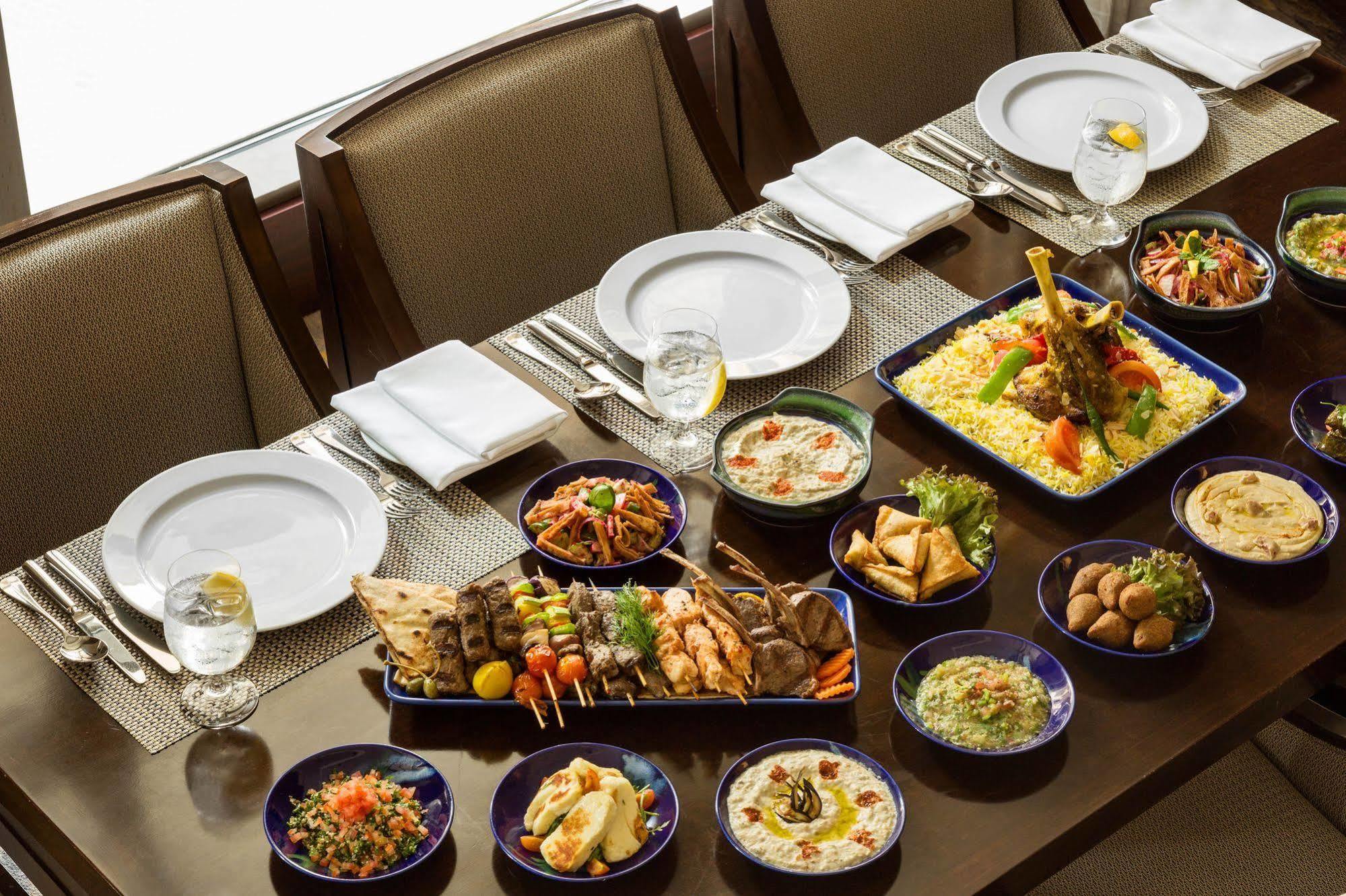 Jabal Omar Hyatt Regency Makkah Hotel Mekka Kültér fotó The photo shows a beautifully arranged dining table set for a feast. There are several plates and dishes filled with a variety of foods:

1. **Main Dishes**: A large platter features grilled meats, including skewers and seasoned chicken, garnished wi