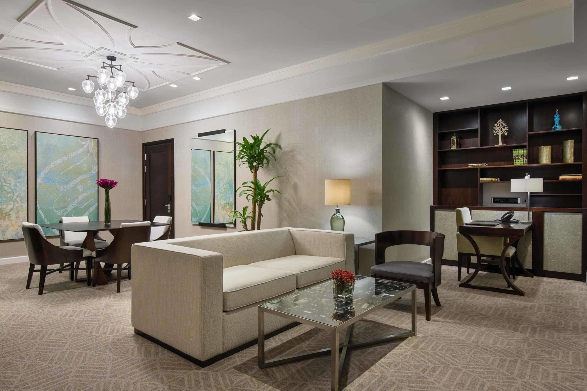 Jabal Omar Hyatt Regency Makkah Hotel Mekka Kültér fotó The image shows a contemporary living space that includes a light-colored sofa and a glass coffee table. In the background, there is a dining area with a round table and chairs, along with framed artwork on the walls. A potted plant adds a touch of g