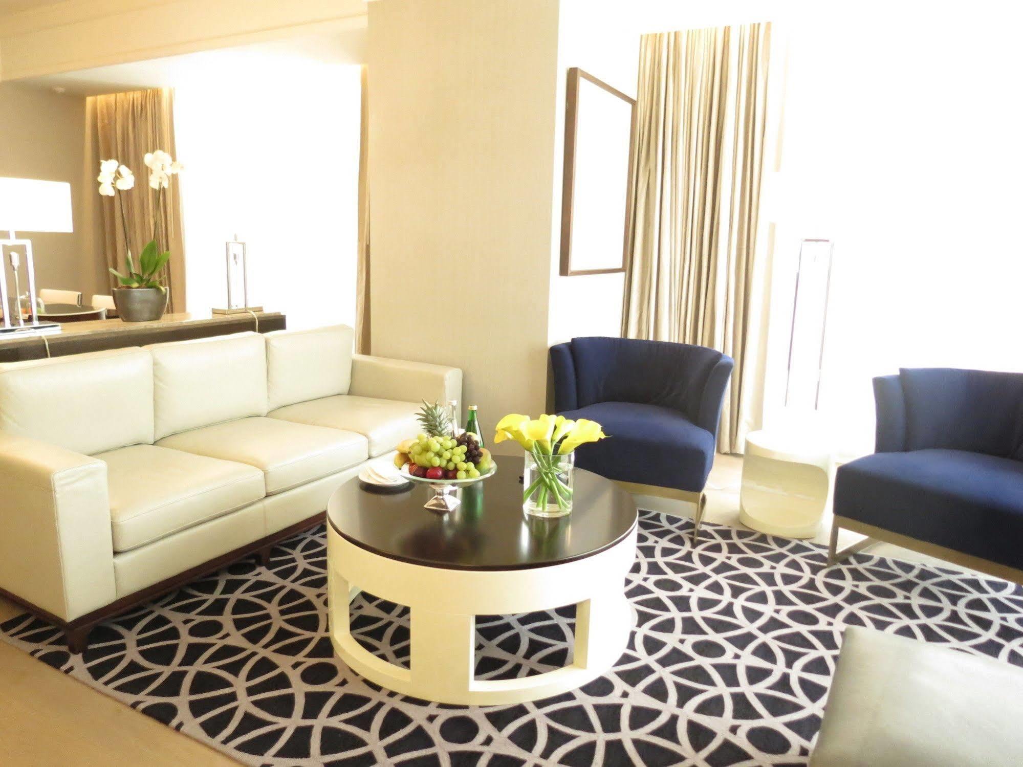 Jabal Omar Hyatt Regency Makkah Hotel Mekka Kültér fotó The photo shows a stylish and modern living area. It features a white sectional sofa, two blue upholstered chairs, and a round black coffee table with a decorative centerpiece that includes flowers and fruits. The flooring is covered with a patterned
