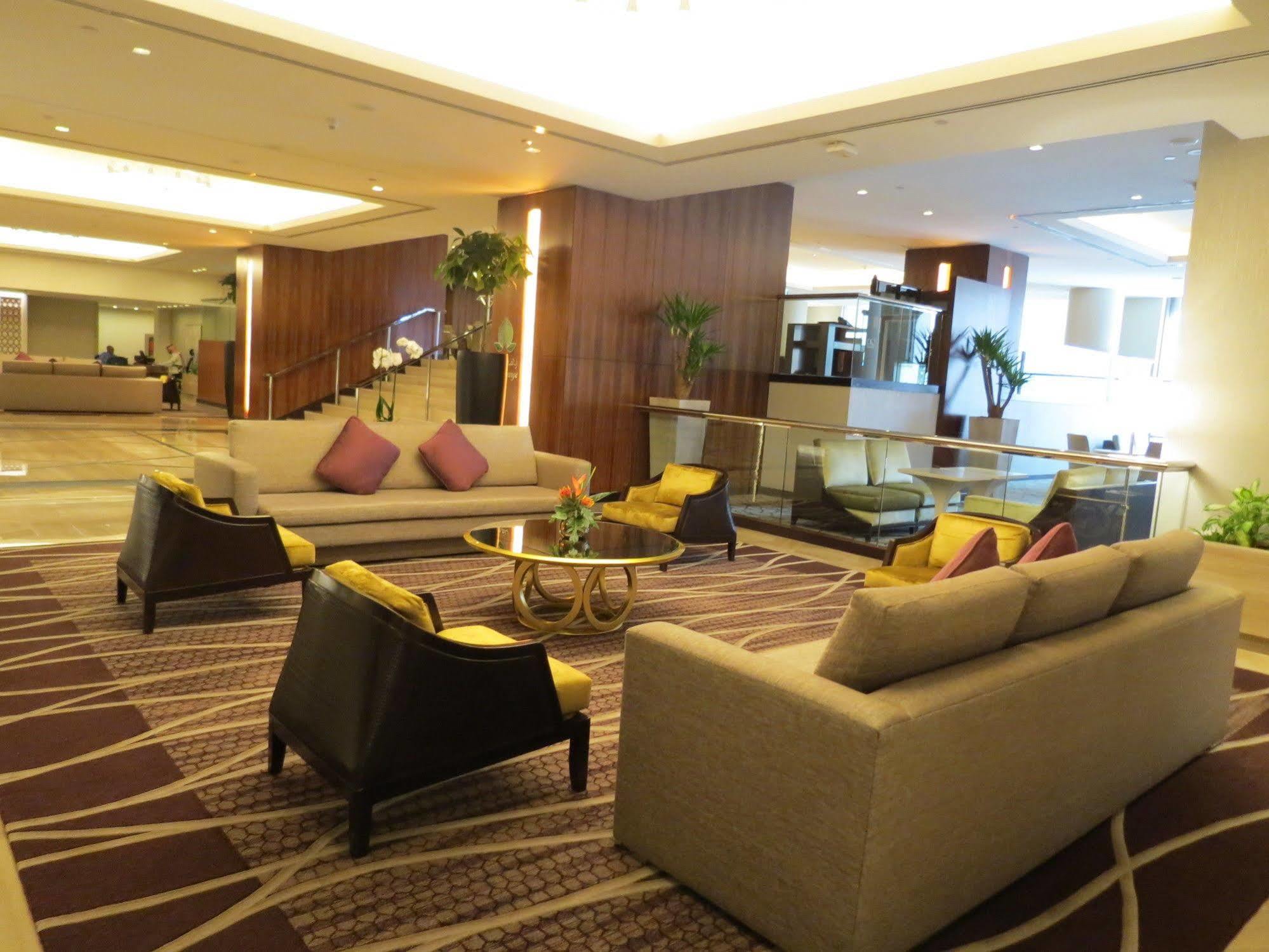 Jabal Omar Hyatt Regency Makkah Hotel Mekka Kültér fotó The photo shows a modern and stylish lobby or lounge area. It features two large sofas with a light color and several cushions in shades of purple. There are also two armchairs with a darker finish and yellow cushions. In the center, there is a round