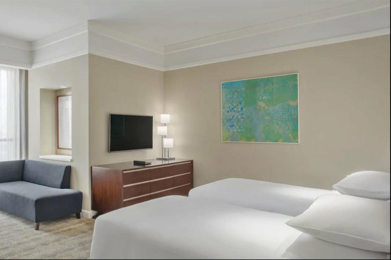 Jabal Omar Hyatt Regency Makkah Hotel Mekka Kültér fotó The photo shows a hotel room featuring two twin beds with white bedding. A dark wooden dresser is positioned against one wall, with a flat-screen TV mounted above it. Next to the dresser, there are two modern lamps providing soft lighting. On the wal