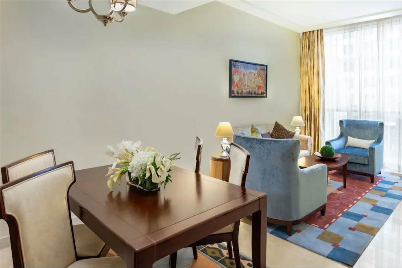 Jabal Omar Hyatt Regency Makkah Hotel Mekka Kültér fotó The photo shows an elegantly furnished living space. On the left, there's a wooden dining table with four chairs, decorated with a vase of white flowers. To the right, there are two comfortable blue armchairs and a small side table, each adorned with